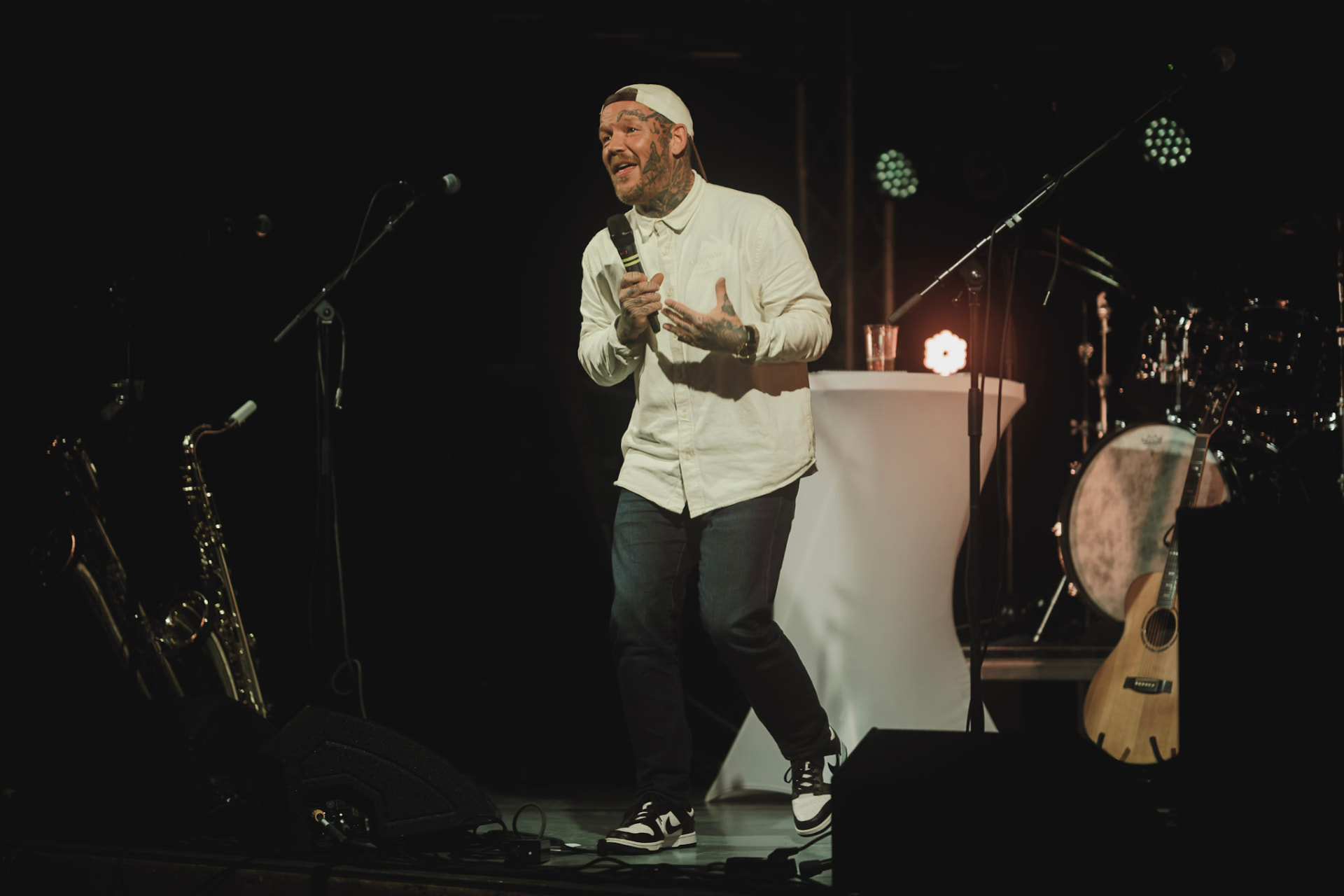 Komiker med mikrofon på scenen mellom musikkinstrumenter