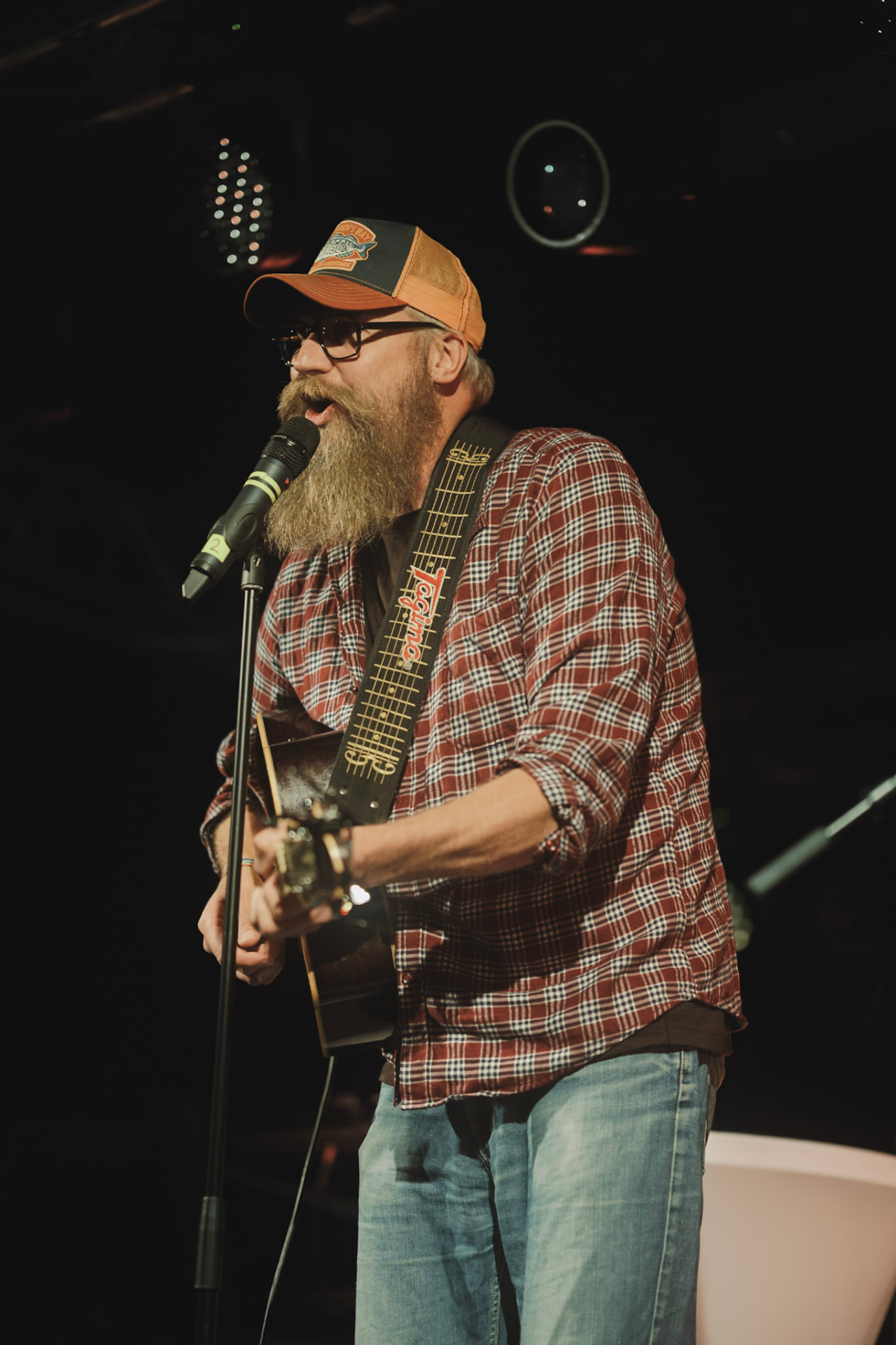 Musiker med gitar og skjegg synger i mikrofonen på scenen